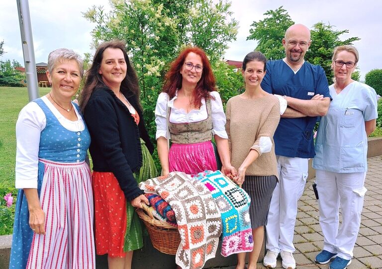 Kolleg*innen aus dem Clementinum und Vertreter*innen der Wollweiber halten einen Korb mit selbst gehäkelten Wolldecken.