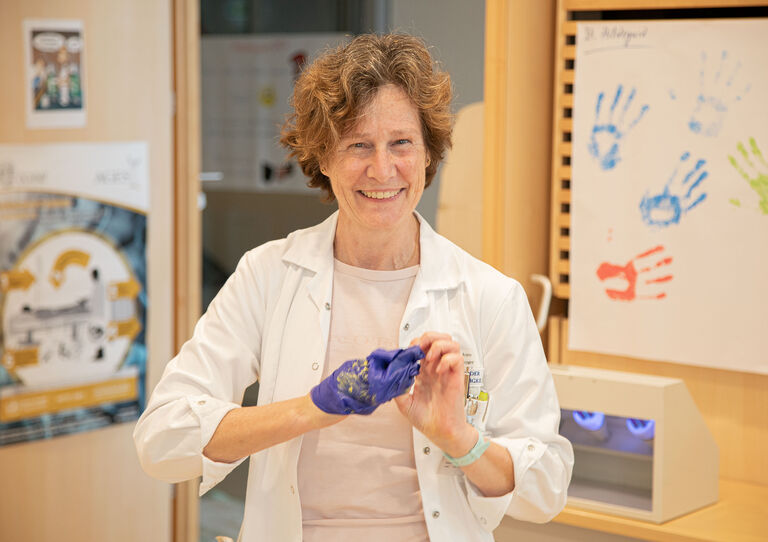 Eine Kollegin zieht ihren Handschuh aus und lächelt in die Kamera