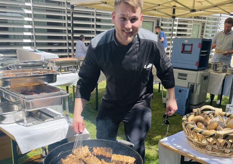 Kollege steht hinter dem Kugelgriller und grillt