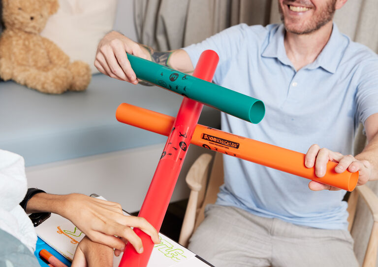 Mitarbeiter und Kunde halten drei bunte Stangen eines Spiels zusammen. Man sieht nur einen Teil des Gesichts des Mitarbeiters und die Hände des Kunden. Mitarbeiter und Kunde halten drei bunte Stangen eines Spiels zusammen. Man sieht nur einen Teil des Gesichts des Mitarbeiters und die Hände des Kunden.