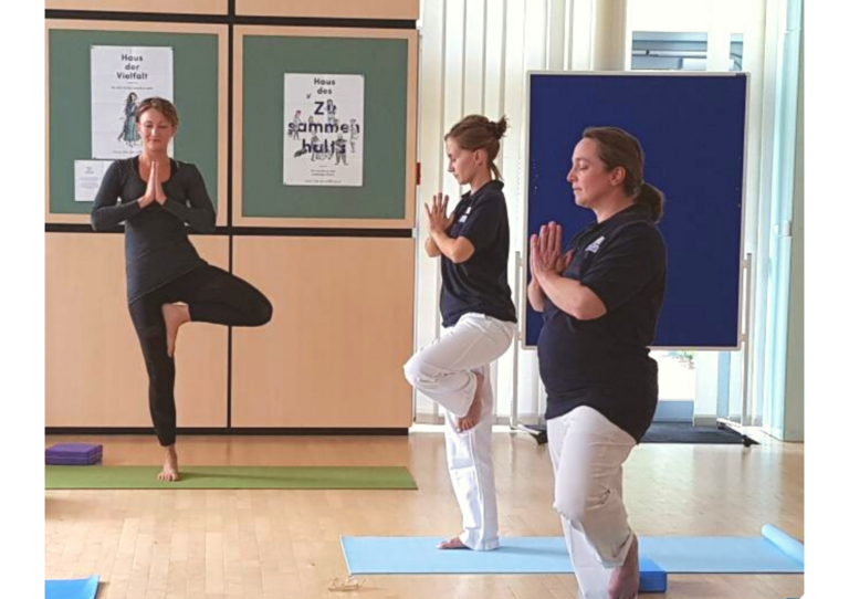 Drei HB Kolleg*innen machen Yoga auf einer Yogamatte.