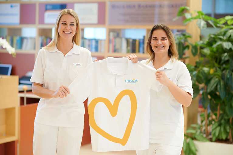 Die Leiter*innen von FRIDOLINA halten ein Team-T-Shirt des Kinderpflegedomizils hoch.