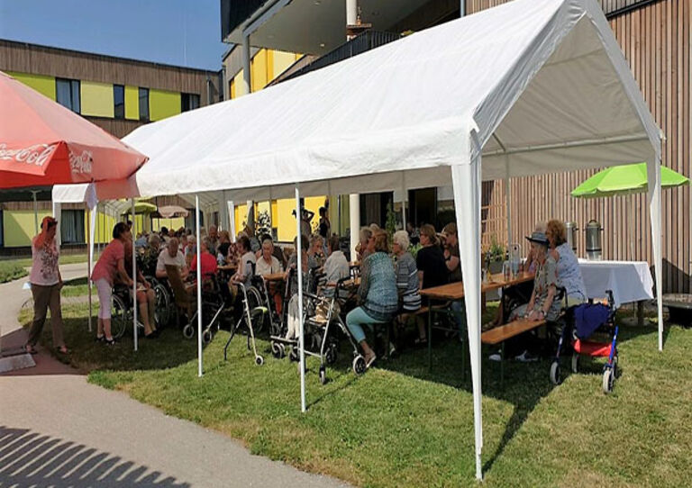 BewohnerInnen und MitarbeiterInnen genießen im Garten Grillspezialitäten.