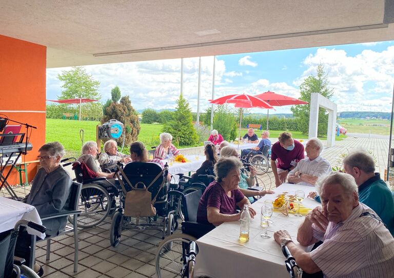 Bewohner*innen aus dem Clementinum sitzen auf mehreren Tischen, plaudern miteinander und nehmen Essen und Getränke zu sich.