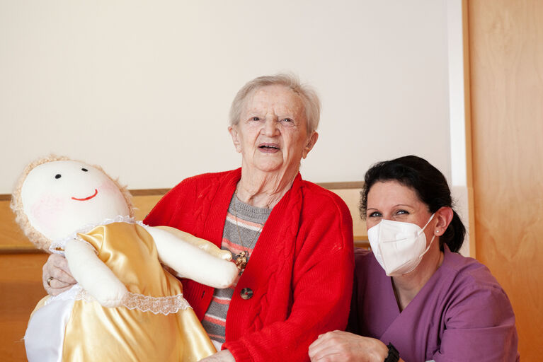 Bewohnerin Elsa hält einen Schutzengel und Bewohnerin Daniela kniet daneben.