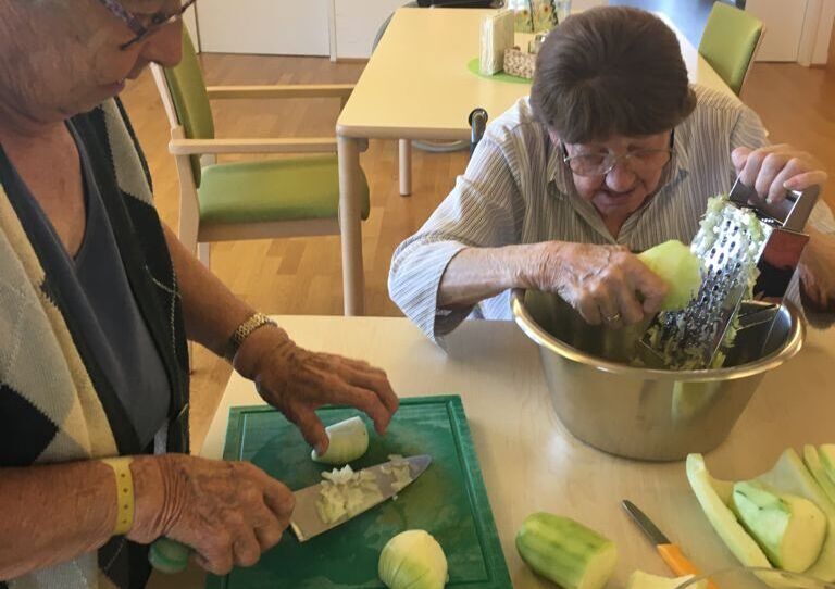 Zwei Bewohnerinnen schälen und reiben Zucchinis auf