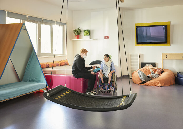Ein Mitarbeiter sitzt dem Kunden gegenüber, man sieht davor eine Nestschaukel. Sie sind im Bewegungsraum.