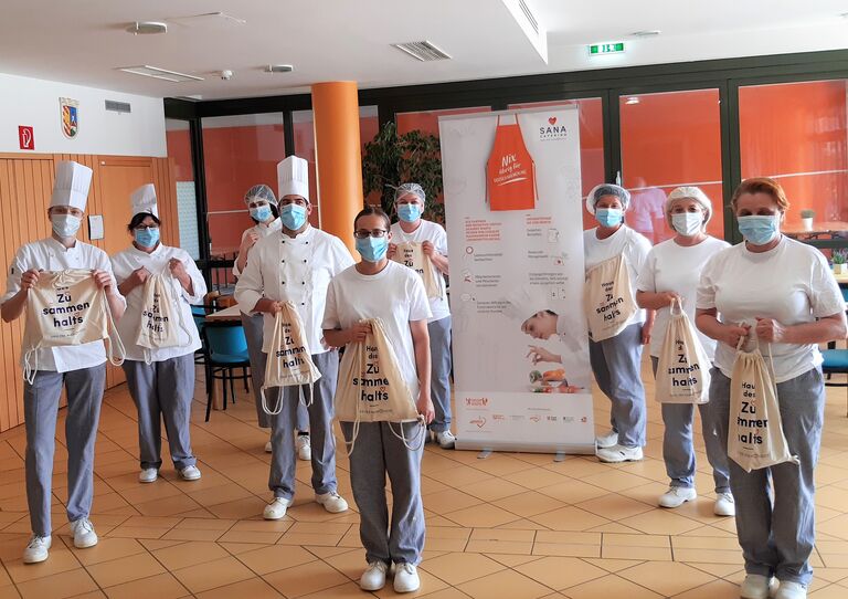 Das SANA Team mit Tragetaschen mit der Aufschrift Haus des Zusammenhalts.