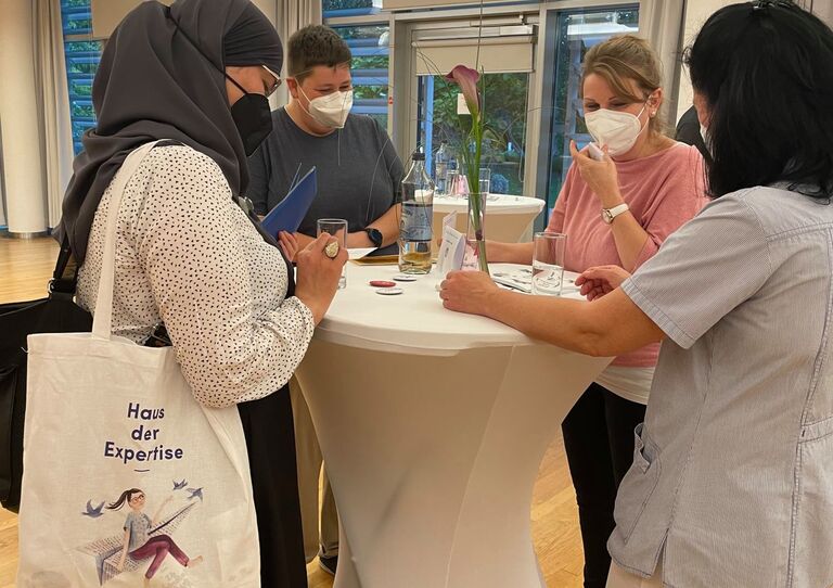 Zwei Mitarbeiter*innen plaudern mit zwei Interessent*innen an einem Tisch.