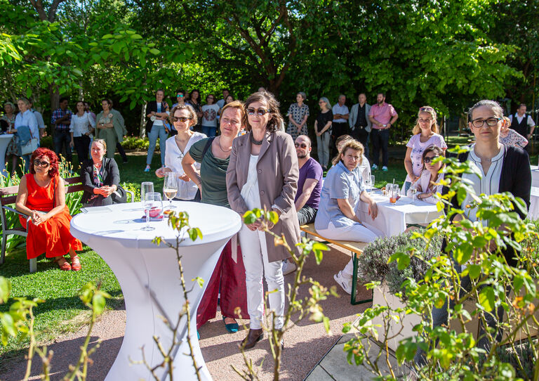 Mitarbeiter*innen verfolgen die Ansprachen bei der Eröffnung