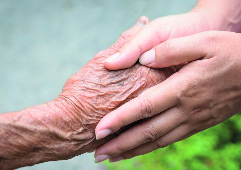 Die Hände eines jungen Menschen halten die Hand eines älteren.
