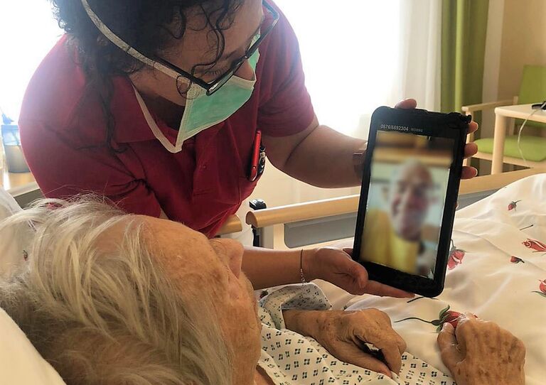 Eine Pflegerin hält das Tablet für eine Bewohnerin im Krankenbett.