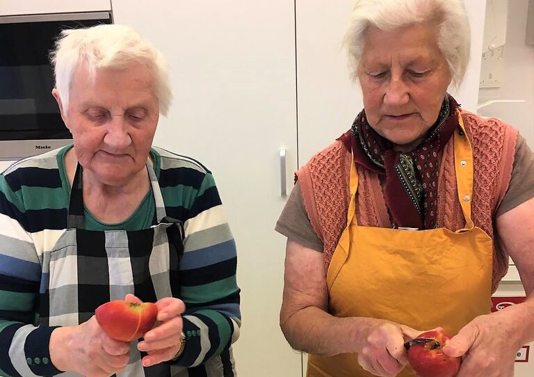 Zwei Bewohnerinnen schneiden das geerntete Obst und Gemüse.