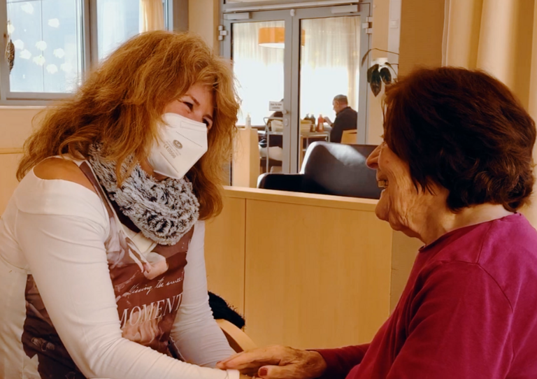 Eine Mitarbeiterin hält eine Bewohnerin, die von hinten zu sehen ist, an den Händen