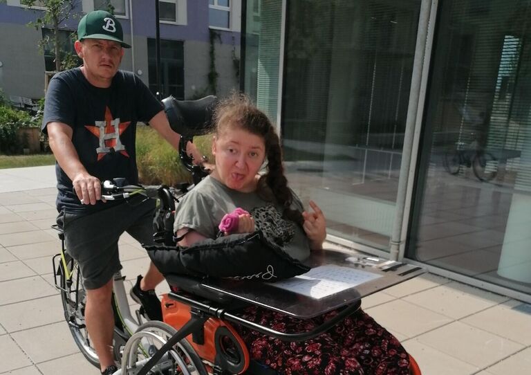 HABIT Kollege auf einem speziellen rollstuhlgerechten Lastenfahrrad, auf dem eine Kundin im Rollstuhl sitzt.