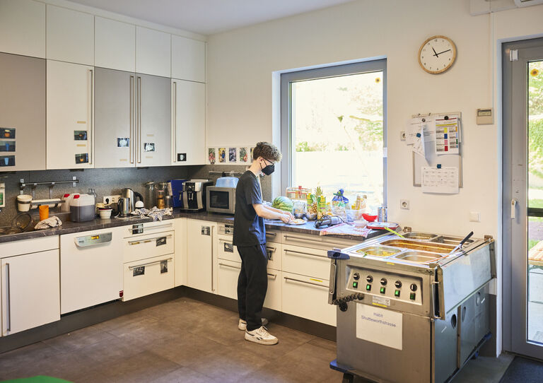 Mitarbeiter kocht in der Küche. Man sieht ihn seitlich von hinten.