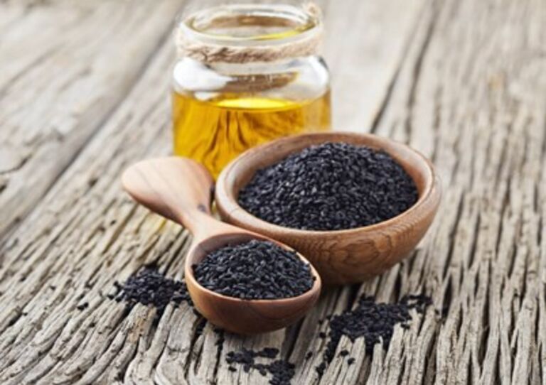 Ein kleines Fläschchen Schwarzkümmelöl und davor zwei Holzlöffel gefüllt mit puren Schwarzkümmel