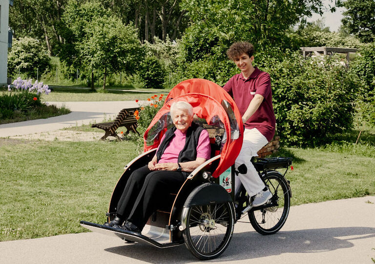 Zivildiener fährt E-Rikscha, Bewohnerin sitzt im Sitzkorb