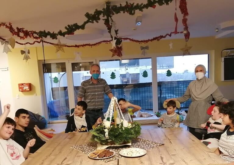Die Kinder der Kids WG sitzen am Tisch rund um einen schönen Adventkranz und lächeln in die Kamera.