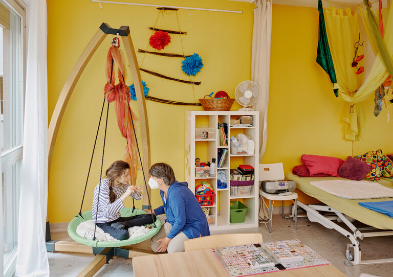 BTZ Lobenhauerngasse: Eine Kundin sitzt in einer Nestschaukel und eine Mitarbeiterin schaukelt sie an. 