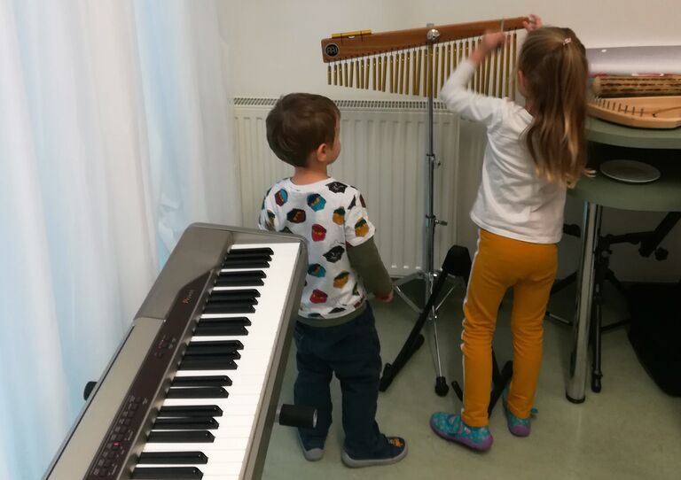 Zwei Kinder probieren das Chime aus, ein Instrument, das aus verschieden langen hängenden Klangstäben besteht.