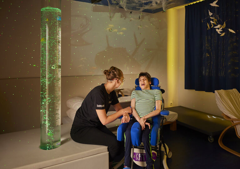 Eine Mitarbeiterin neben einer Kundin im Rollstuhl im Snoezelen-Raum