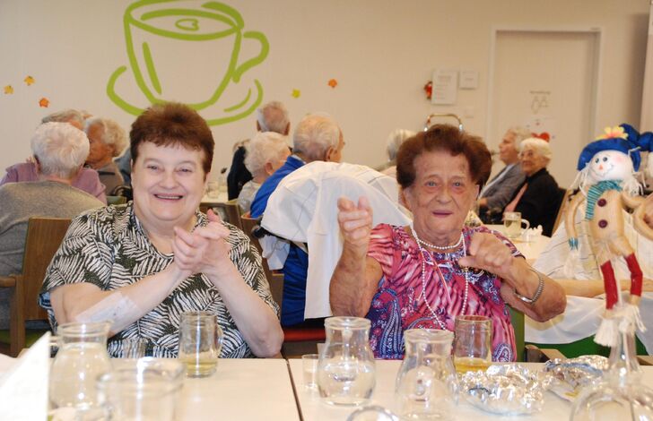 Zwei Bewohnerinnen sitzen an einem Tisch und klatschen und schunkeln mit.