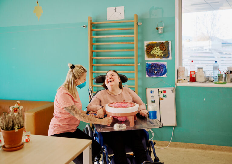 (ZAB), 21. Bezirk: eine Mitarbeiterin sitzt neben einer Kundin im Rollstuhl, die Kundin lächelt die Mitarbeiterin an. 