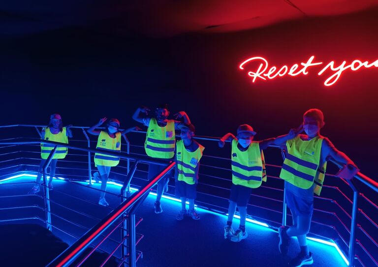 HB Ferienbetreuung: Kinder mit Leuchtwesten in dunklem Raum. Kinder mit Leuchtjacken im Dunkeln.