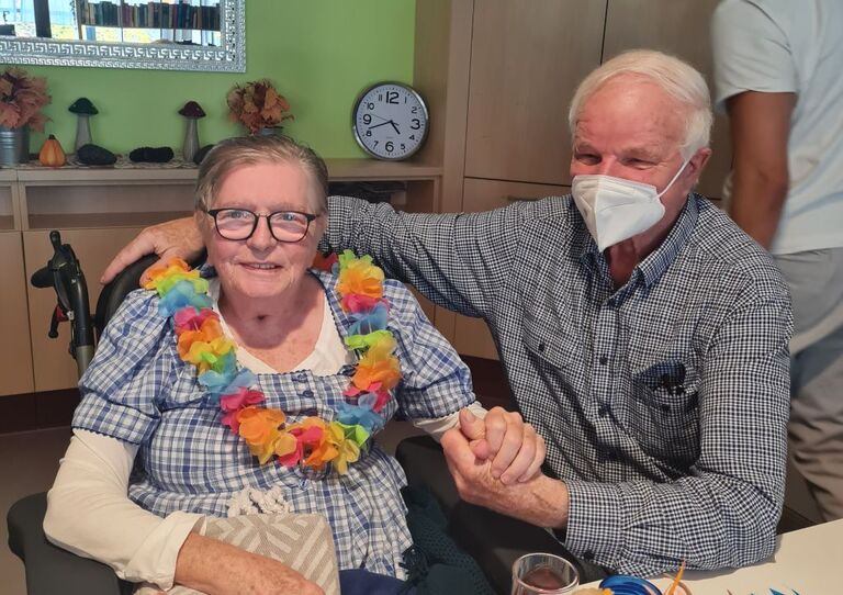 Eine Bewohnerin und ein Angehöriger sitzen mit einer Brezen am Tisch