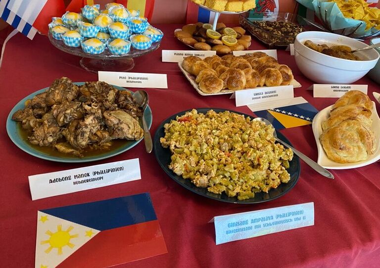 Ein Foto vom Buffet mit lauter Speisen aus der internationalen Küche. Außerdem kleine Fähnchen und andere Dekoration.