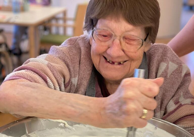 Bewohnerin Katharina rührt lächelnd einen Teig.