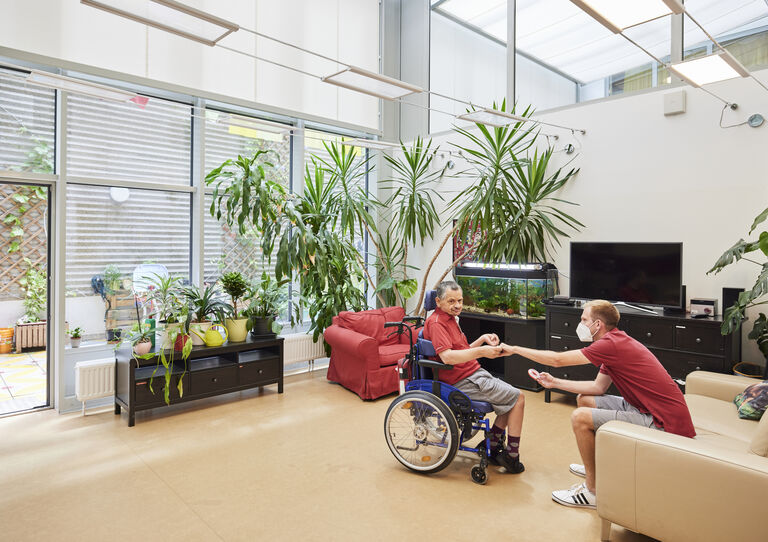 Im Wohnzimmer im GV Verbund Triester Straße sitzen ein Kunde und ein Mitarbeiter und reichen sich die Hand.