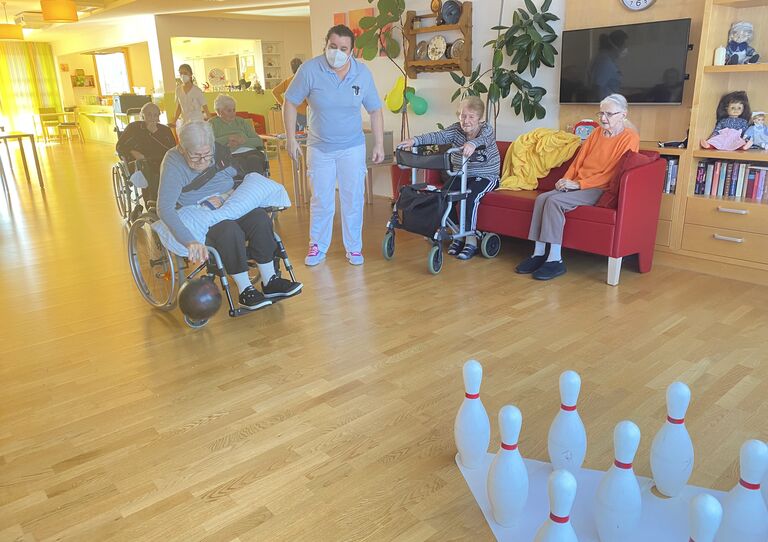 Eine Bewohnerin im Rollstuhl holt zum Wurf aus. Andere Bewohnerinnen schauen zu.
