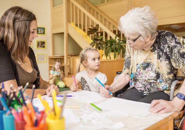 Szene Kindergarten: Mutter sitzt neben einem kleine Mädchen und dieses blickt zu einer Bewohnerin auf.