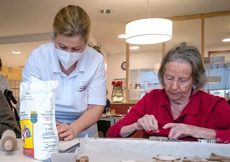 Eine Bewohnerin und eine Mitarbeiterin stechen Kekse aus.