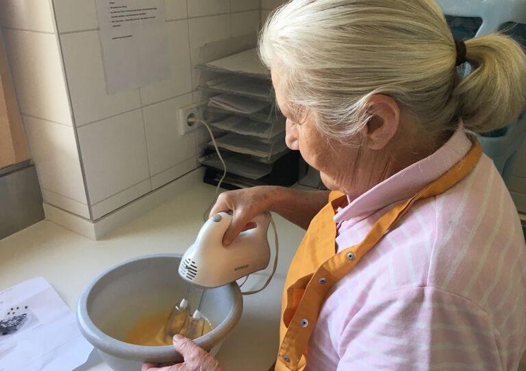 Eine Bewohnerin bereitet den Teig von Zucchinikuchen vor. Eine zweite Bewohnerin unterstützt sie.