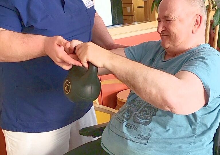 Bewohner trainiert mit Hantel und bekommt Hilfe von Mitarbeiterin.