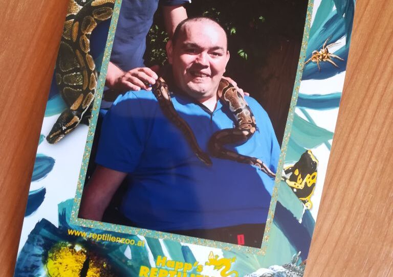 Ein Foto eines Fotos, auf dem ein Kunde freundlich lächelt und eine Schlang um den Hals gelegt bekommt.