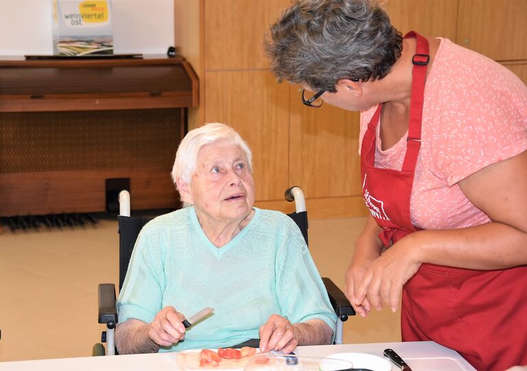 Eine Bewohnerin schneidet Tomaten und unterhält sich mit einer Seminarbäuerin.