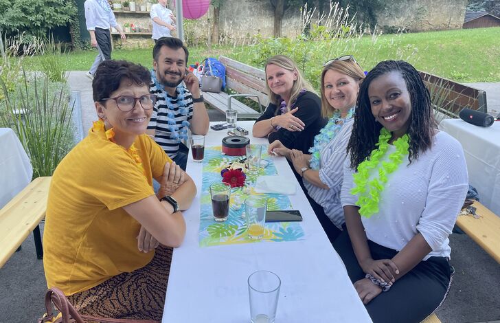 Einige Mitarbeiter*innen vom AMB sitzen an einem tisch und tragen Hawaiketten