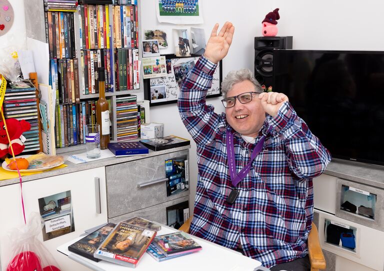 Ein Kunde sitzt an seinem Tisch in seinem Zimmer und streckt fröhlich die Hände in die Höhe.