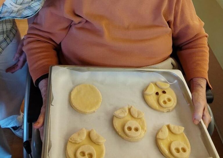 Eine Bewohnerin und eine Mitarbeiterin mit dem Backblech, auf dem die Schweinchen sind.