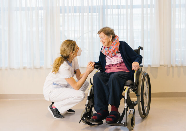 Pflegeberaterin Karin Haubenwaller hält die Hand unserer Bewohnerin Nadja Ehnhofer, die im Rollstuhl sitzt.