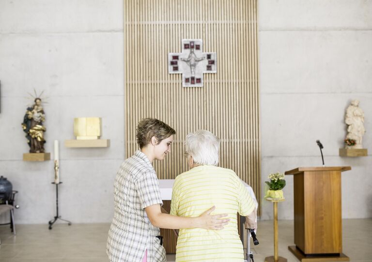 Eine Mitarbeiterin stützt eine Bewohnerin in der Kapelle.