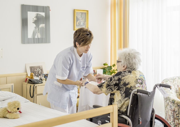Mitarbeiterin hilft Bewohnerin beim Aufstehen aus dem Rollstuhl