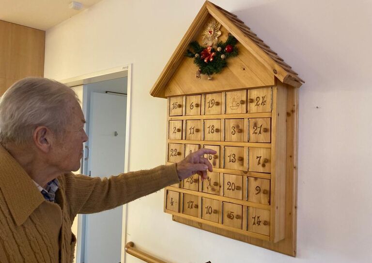 Ein Bewohner öffnet ein Türchen aus dem Adventkalender, er ist aus Holz und hat eine Ähnlichkeit mit dem Häuschen von einer Kuckucksuhr.