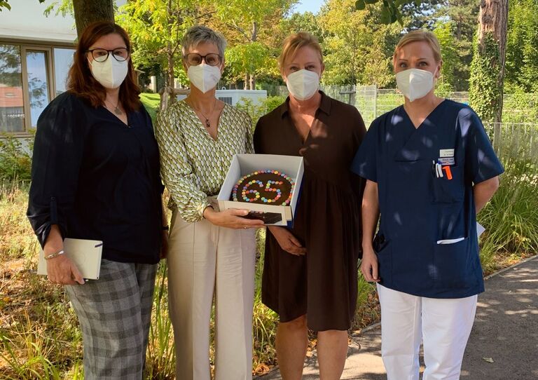 Vier Kolleg*innen Am Maurer Berg stehen zusammen im Garten und halten eine Geburtstagstorte in den Händen.