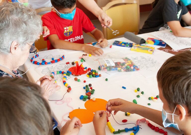 Ein Bub bastelt mit einer Bewohnerin eine Kette.