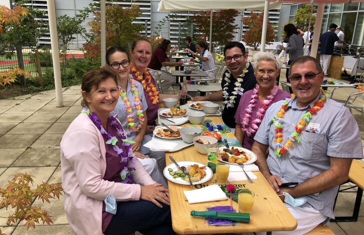 Gruppenfoto von Mitarbeiter*innen der Tokiostraße. Sie sitzen an einem Biertisch und tragen Hawaiketten.